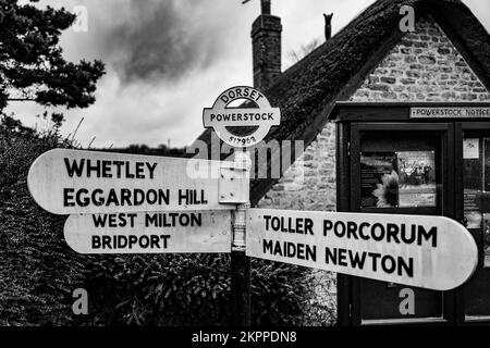 Öffentlicher Beschilderung zur Oldtimer-Straße in Dorset. Der Posten steht vor dem Powerstock Village Hinweisschild und der Hütte. Schwarzweißfoto. Stockfoto