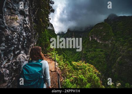 Beschreibung: Wunderschöne Frau mit Rucksack bewundert die Aussicht vom abenteuerlichen Dschungelweg entlang des Kanals. Levada Caldeirão Verde, Madeira Stockfoto