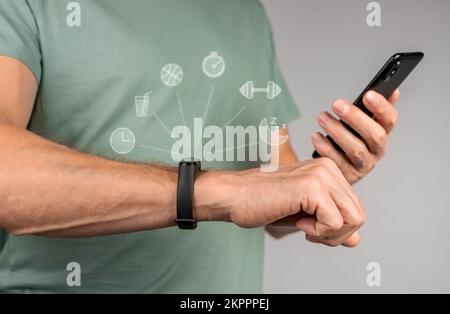 Mit fitbit, Fitnessarmband und Mobiltelefon. Hände mit Sport-Smartwatch und Smartphone für Synchronisation. Hochwertiges Foto Stockfoto