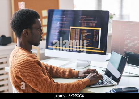 Seriöser junger Schwarzer in warmem orangefarbenem Pullover, konzentriert sich auf Kodierung Stockfoto