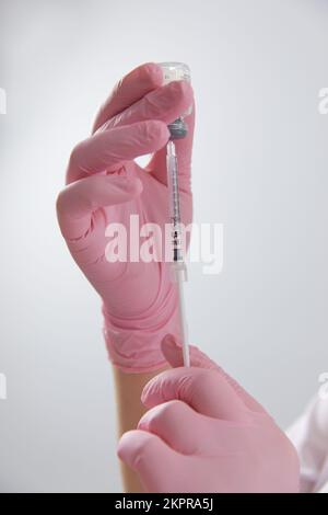 Hände in blauen medizinischen Handschuhen zeichnen eine Spritze mit covid-19-Impfstoff aus einem Fläschchen, Kopierraum, Nahaufnahme. Impfkonzept für Coronaviren. Stockfoto