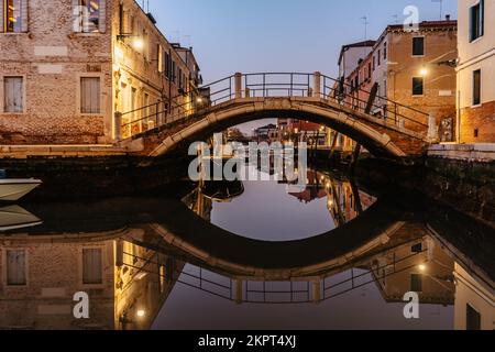 Wasserkanal, Brücke in der Dämmerung, Venedig, Italien. Typischer Bootstransport, venezianische Reise, städtische Szene. Wassertransport. Beliebtes Touristenziel. Romantisch Stockfoto