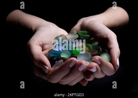 Hände mit farbigen Steinen die junge Frau hält eine Sammlung verschiedener roher mineralischer Edelsteine in ihrer Handfläche, isoliert auf schwarzem Hintergrund Stockfoto