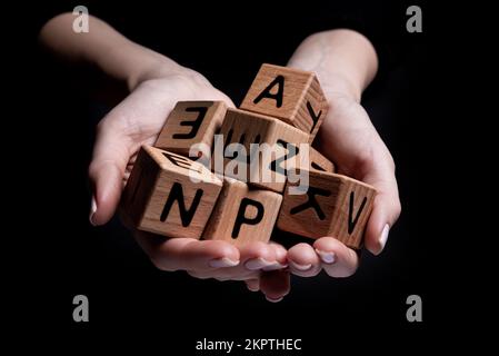 Weibliche Hände halten einen Würfel mit isolierten Buchstaben auf schwarzem Hintergrund Stockfoto