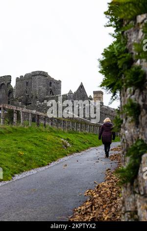 Frau in brauner Jacke, die auf dem Weg in der Nähe von Rock of Cashel, Castle on the Hill in Tipperary, Irland, spaziert Stockfoto