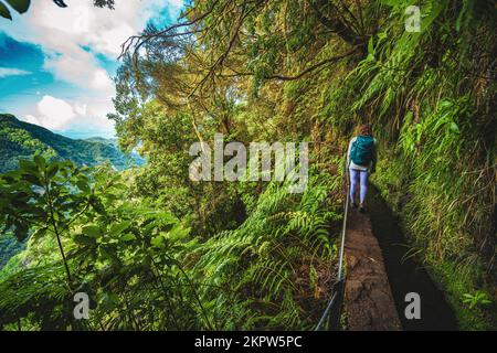 Beschreibung: Wunderschöne Frau mit Rucksackwanderungen auf abenteuerlichem Dschungelweg entlang des Wasserkanals. Levada von Caldeirão Verde, Insel Madeira, Portugal, EU Stockfoto