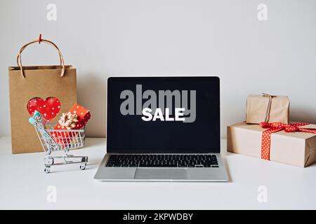 Valentinstag-Angebot Erfolgreich. Valentinstag Online-Shopping, E-Commerce. Offener Laptop Bildschirm, Mini-Einkaufswagen, Einkaufstaschen Stockfoto