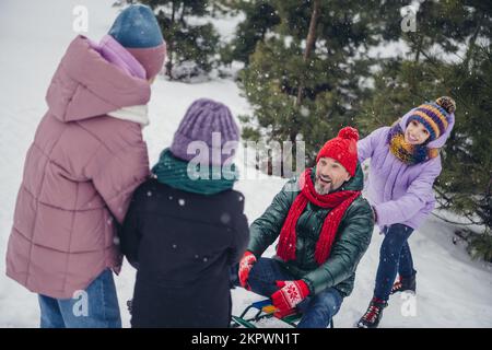 Foto von vier sorglosen, fröhlichen Menschen, die draußen Schlittenfahrten und Schneefallwetter genießen Stockfoto