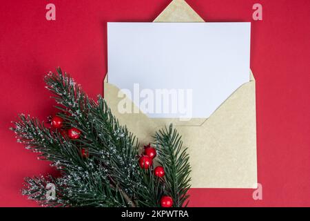 Weihnachtspostkarte oder Weihnachtsbrief in goldenem Umschlag auf rotem Hintergrund mit Kopierbereich und Fichtenholz und roten Heidelbeeren. Stockfoto