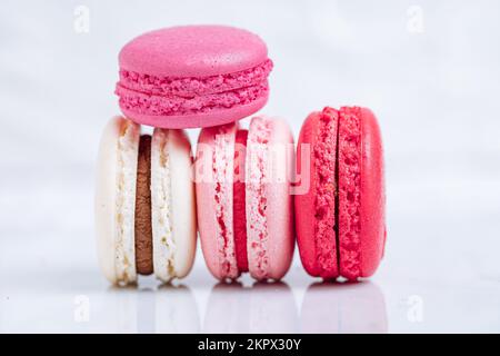 Nahaufnahme von Makronen in verschiedenen Farben auf hellem weißem Hintergrund mit dezenter Reflexion auf Marmorschale. Beliebtes Merengue-Dessert mit Füllungen Stockfoto