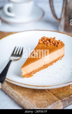 Ein Stück Karamell-Käsekuchen mit Kekskrümeln. Cremiger, dreischichtiger Kuchen auf hellen Tellern. Beliebtes amerikanisches Dessert. Stockfoto