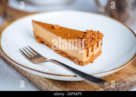 Ein Stück Karamell-Käsekuchen mit Kekskrümeln. Cremiger, dreischichtiger Kuchen auf hellen Tellern. Beliebtes amerikanisches Dessert. Stockfoto