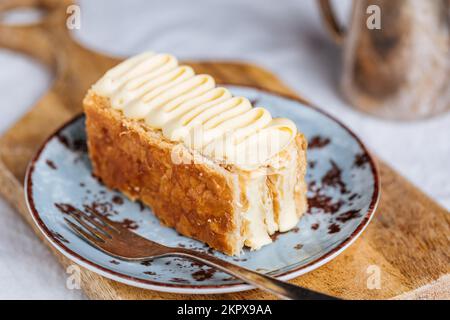 Französisches Dessert namens Mille Feuille oder Napoleon Kuchen auf rustikalem Holzbrett. Mehrlagiger leckerer Kuchen mit Vanillecreme und Blätterteig. Stockfoto