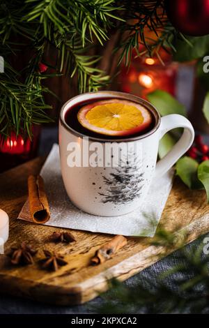 Glühwein mit Zimt und Orange, serviert in festlicher Weihnachtsdekoration auf Holzbrettern. Party- und Silvesteratmosphäre. Weihnachtsbaum im Backgrou Stockfoto