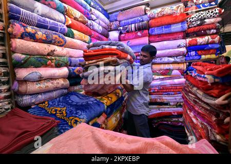 Dhaka. 28.. November 2022. Ein Mann arrangiert chinesische Decken auf einem Markt in Dhaka, Bangladesch, am 23. November 2022. Die Märkte in Dhaka sind jetzt vor der Hochsaison der Winterverkäufe voll ausgelastet. Dank ihrer Erschwinglichkeit und ihres attraktiven Designs ziehen mittlerweile viele Fachgeschäfte mit einer umfangreichen Sammlung chinesischer Decken viele Kunden an. Kredit: Xinhua/Alamy Live News Stockfoto