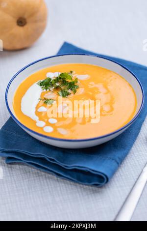 Cremige Kürbissuppe garniert mit Kochsauce, serviert in einer türkisfarbenen Schüssel auf dezentem grauem Hintergrund. Warme Speisen der Saison. Herbstvorspeise Stockfoto