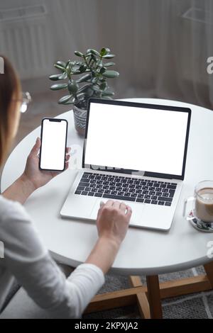 Modell eines Laptops mit weißem Bildschirm und einer Frau, die ihren Computer benutzt, während sie zu Hause am Tisch sitzt, Rückansicht Stockfoto