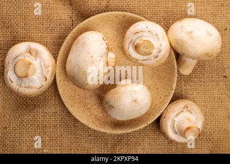 Ein paar ganz organische, frische Pilze Champignon, mit einer Keramikuntertasse, auf einer Juteserviette, Draufsicht. Stockfoto