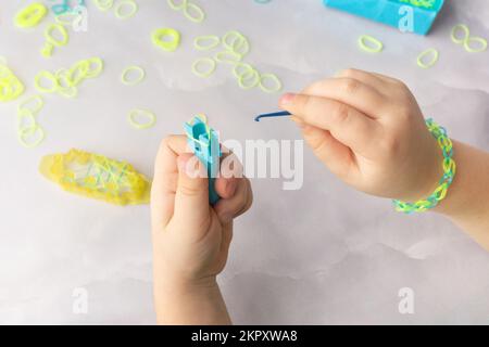 Konzept der Herstellung von Webstubenarmbändern durch Kinder in Blau und Gelb Stockfoto