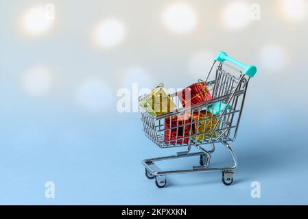 Nahaufnahme eines kleinen Einkaufswagens voller Weihnachtsgeschenke. Unschärfe-Lichter im Hintergrund. Stockfoto