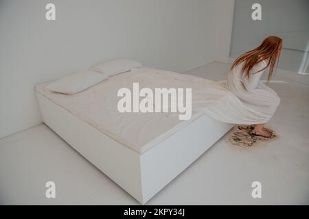 Depressive Frau, die auf einem schmutzigen Bett sitzt Stockfoto