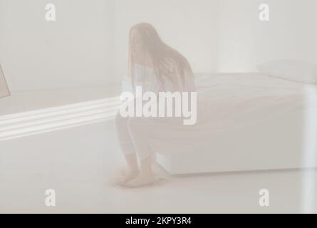 Depressive Frau, die auf einem schmutzigen Bett sitzt Stockfoto