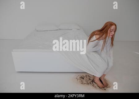 Depressive Frau, die auf einem schmutzigen Bett sitzt Stockfoto