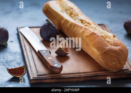 Frisches Baguette mit knuspriger Kruste und Früchten von reifen Feigen auf dem Tisch Stockfoto