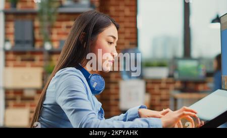 Asiatische Frau, die als Redakteurin mit Grafiktablett und Eingabestift arbeitet und Fotobearbeitungssoftware verwendet, um die Farbskala für die Multimedia-Produktion zu korrigieren. Kreativer Künstler, der Mediendesign entwickelt. Schließen. Stockfoto