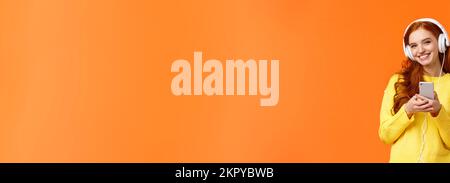 Technologie, Shopping und Personen Konzept. Moderne cute Hipster rothaarige Mädchen tragen weiße Kopfhörer, Smartphone, lächelnd sorglos genießen Sie schöne Stockfoto