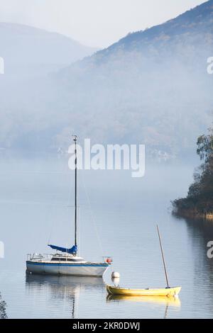 Segelboote, die an einem nebligen Herbstmorgen auf dem Wasser von Coniston festgemacht wurden. Lake District, England, Großbritannien Stockfoto