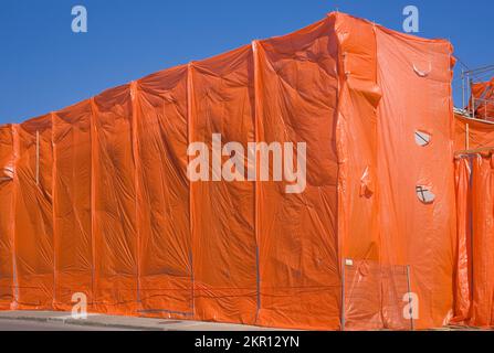 Das Gewerbegebäude ist während der Renovierungsarbeiten mit orangefarbenen Kunststofffolien bedeckt, um Staub und Ablagerungen einzudämmen. Stockfoto