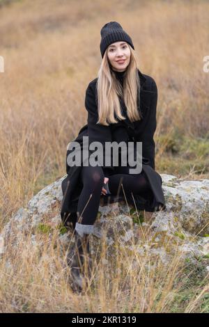 Ein Mädchen in einem schwarzen Mantel sitzt auf einem Berg Stockfoto