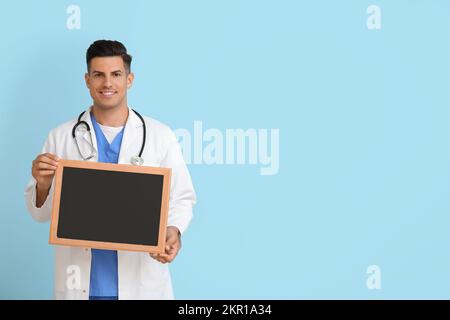 Männlicher Arzt mit schwarzem Brett auf blauem Hintergrund Stockfoto