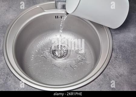 Heißes Wasser gießt aus einem weißen elektrischen Wasserkocher in ein Metallspüle. Schmutzreinigung und -Desinfektion Stockfoto