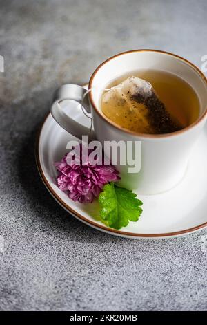 Eine Tasse Tee mit Teebeutel und einer lila Chrysanthemen-Blume auf der Untertasse Stockfoto