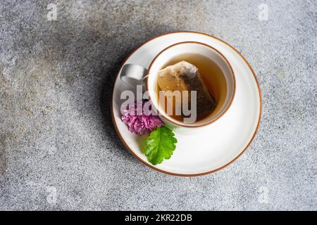 Blick von oben auf eine Tasse Tee mit Teebeutel und einer lila Chrysanthemblume auf der Untertasse Stockfoto