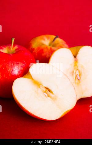 Lebensmittelfoto von roten Äpfeln und Scheiben auf rotem Kartenhintergrund. Stillleben von Apple Stockfoto