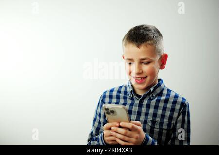 Online-Lernen Soziale Medien Instagram tiktok Boy 9-14 Jahre in einem blauen Karohemd spielt Spiele am Telefon Stockfoto