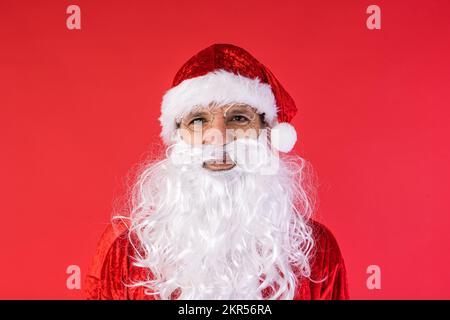 Porträt eines Mannes, verkleidet als Weihnachtsmann, auf rotem Hintergrund. Weihnachten, Feiern, Geschenke, Konsumerismus und Glücksgefühl. Stockfoto