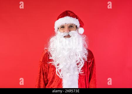 Porträt eines Mannes, verkleidet als Weihnachtsmann, auf rotem Hintergrund. Weihnachten, Feiern, Geschenke, Konsumerismus und Glücksgefühl. Stockfoto