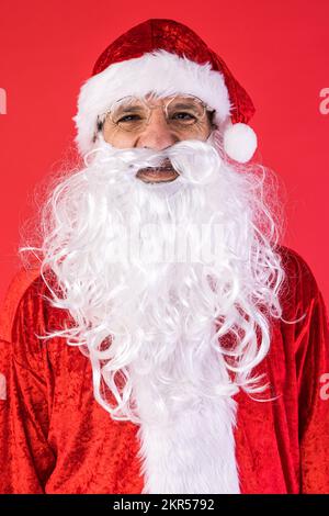 Porträt eines Mannes, verkleidet als Weihnachtsmann, auf rotem Hintergrund. Weihnachten, Feiern, Geschenke, Konsumerismus und Glücksgefühl. Stockfoto