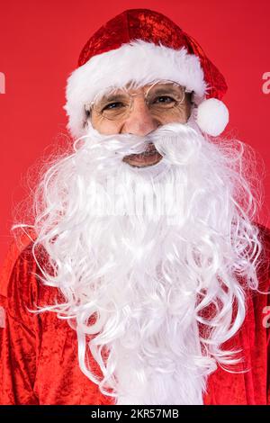 Porträt eines Mannes, verkleidet als Weihnachtsmann, auf rotem Hintergrund. Weihnachten, Feiern, Geschenke, Konsumerismus und Glücksgefühl. Stockfoto