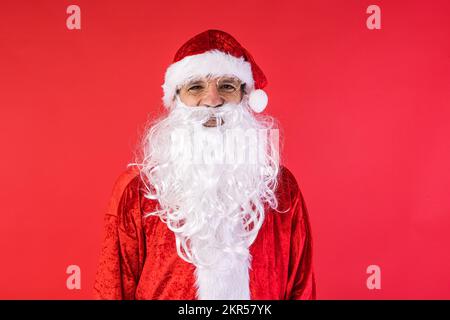 Porträt eines Mannes, verkleidet als Weihnachtsmann, auf rotem Hintergrund. Weihnachten, Feiern, Geschenke, Konsumerismus und Glücksgefühl. Stockfoto