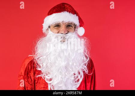 Porträt eines Mannes, verkleidet als Weihnachtsmann, auf rotem Hintergrund. Weihnachten, Feiern, Geschenke, Konsumerismus und Glücksgefühl. Stockfoto