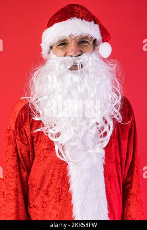 Porträt eines Mannes, verkleidet als Weihnachtsmann, auf rotem Hintergrund. Weihnachten, Feiern, Geschenke, Konsumerismus und Glücksgefühl. Stockfoto