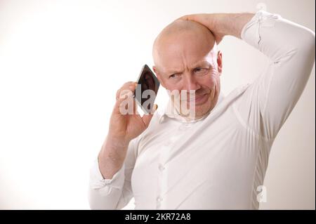 Ein erwachsener Mann in einem weißen Hemd packte sich den Kopf und ist verärgert, dass er die Nachrichten vom Telefongespräch mit einem älteren Mann hört, der sich über das Telefongespräch ärgert, weil er schlechte Nachrichten hört Stockfoto