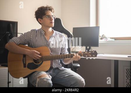 Männlicher Teenager singt Lied spielt akustische Gitarre und liest Text auf dem Smartphone-Anwendungsbildschirm Stockfoto