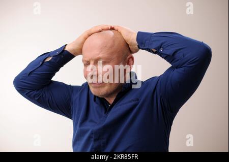 Die Emotionen eines erwachsenen, gutaussehenden, kahlköpfigen Kopfschmerz-Mannes legten seine Hände auf den Kopf und schlossen seine Augen ein unangenehmes Gefühl, das Medikamente gegen Migräne braucht Stockfoto