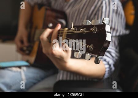 Männlicher Teenager singt Lied spielt akustische Gitarre und liest Text auf dem Smartphone-Anwendungsbildschirm Stockfoto